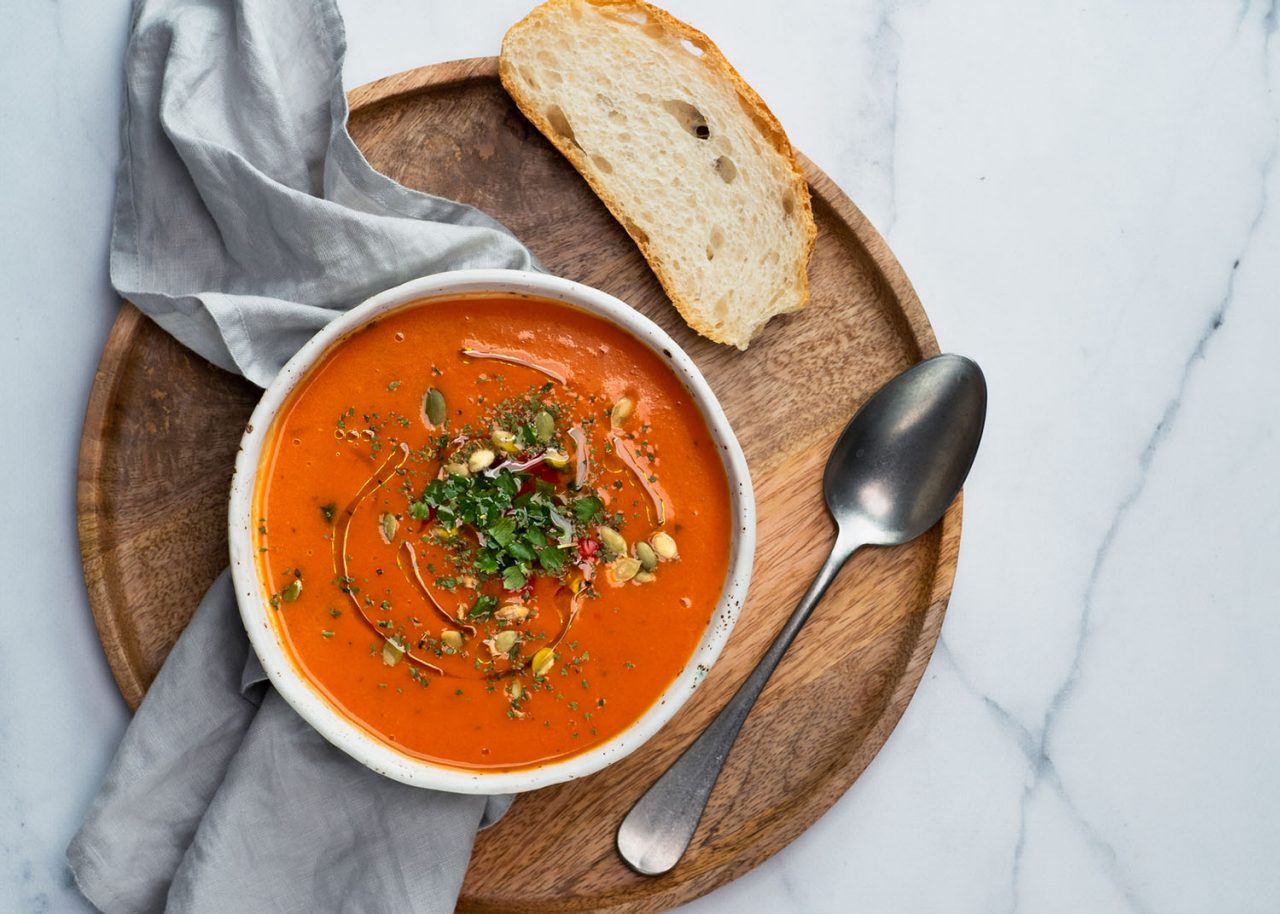 Gaspacho soup on round wooden tray over white marble tabletop. Bowl of traditional spanish cold soup puree gazpacho on light marble background. Copy space for text or design. Top view or flat lay.