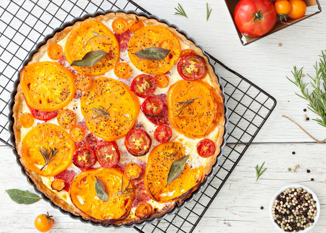 An overhead close up shot of a homemade tomato tart sitting on a metal cooling rack.