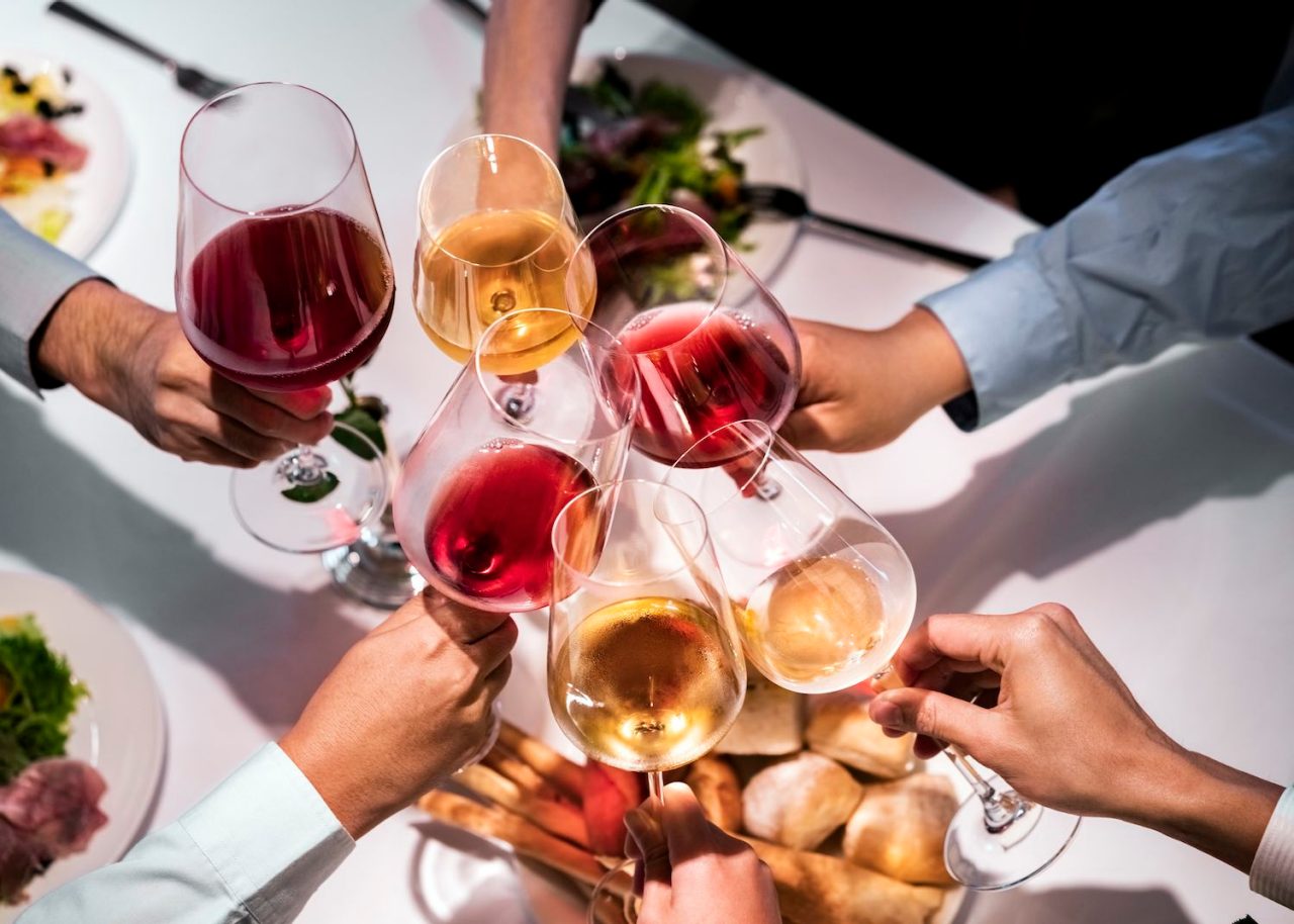 High angle view of cropped hands clinking wineglasses over dining table. Male and female executives celebrating success during business lunch. They are enjoying at restaurant.