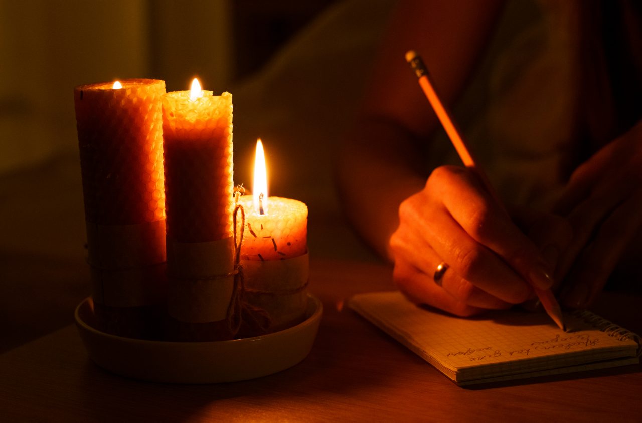 A woman makes notes in a notebook in a dark room with burning candles. Close-up. Magic and occultism.