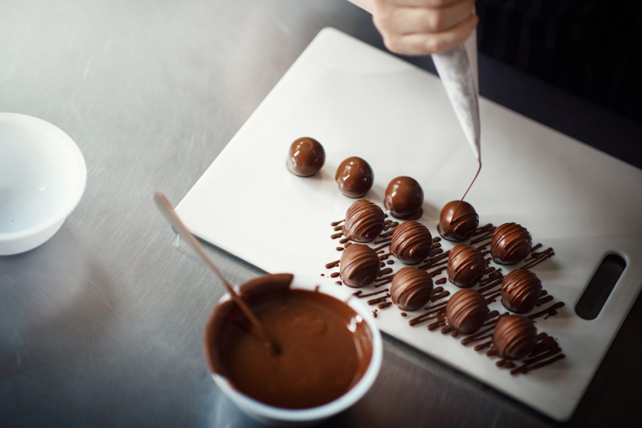 Closeup of a woman putting melted chocolate icing over chocolate truffles.