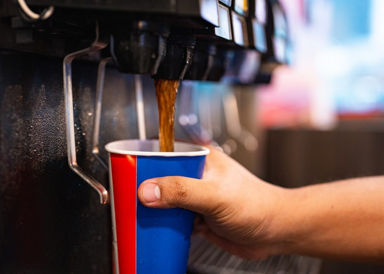 Man holding a cup at soft drink self service machine pouring cola fizzy drink at a restaurant.
