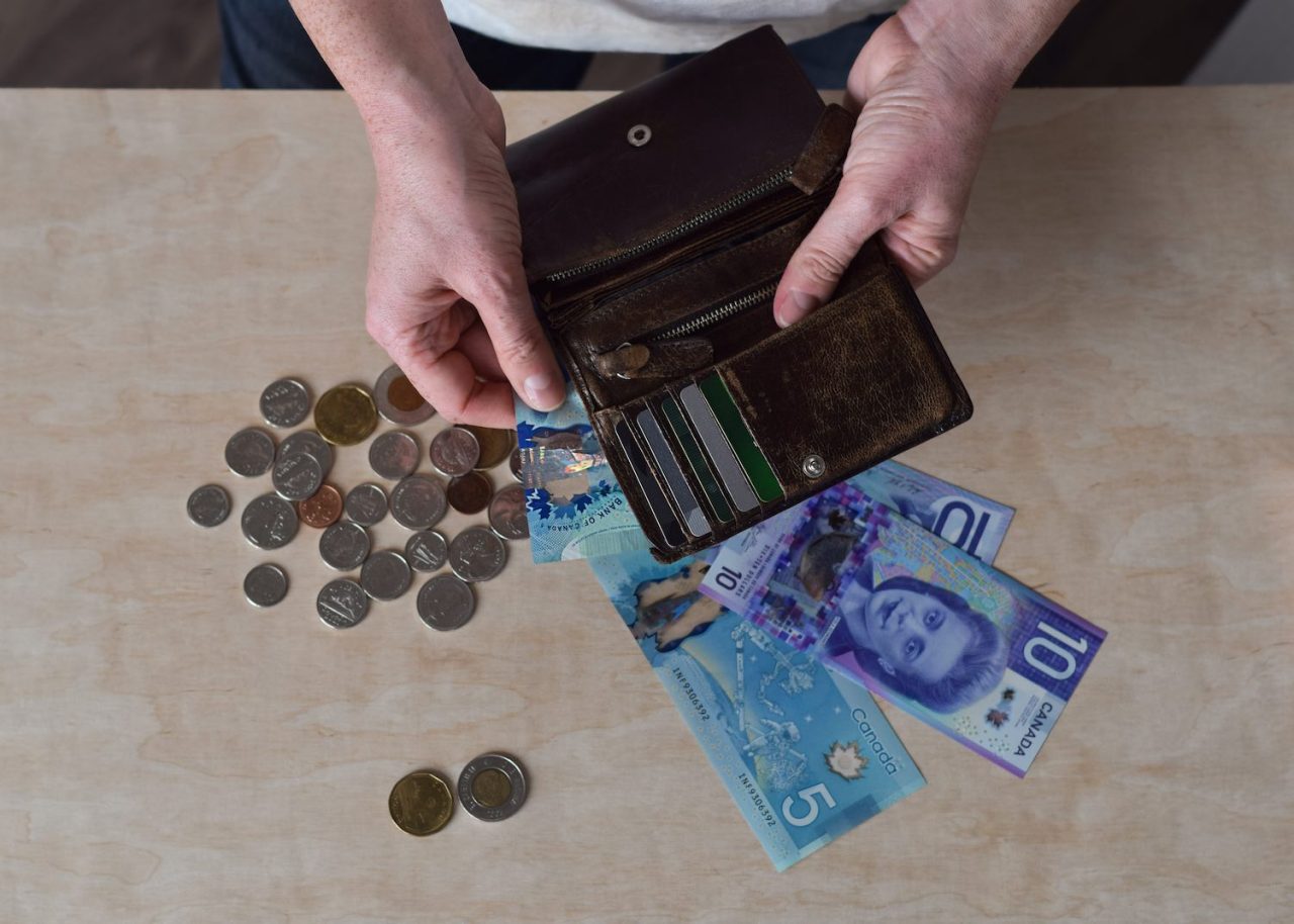 Female hands holding brown wallet counting and paying with Canadian cash dollars and coins