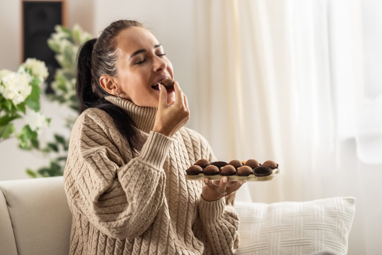 A young woman couldn't resist the sweet temptation to eat chocolate candies and enjoys them with her eyes closed.