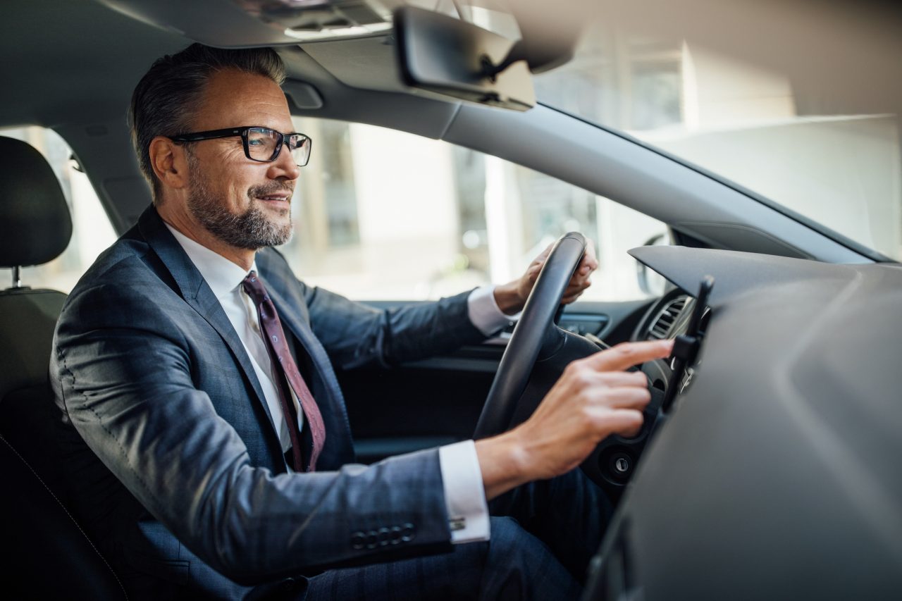 Mature man behind the steering wheel of a car using mobile phone. Businessman using navigation on smart phone in the car.