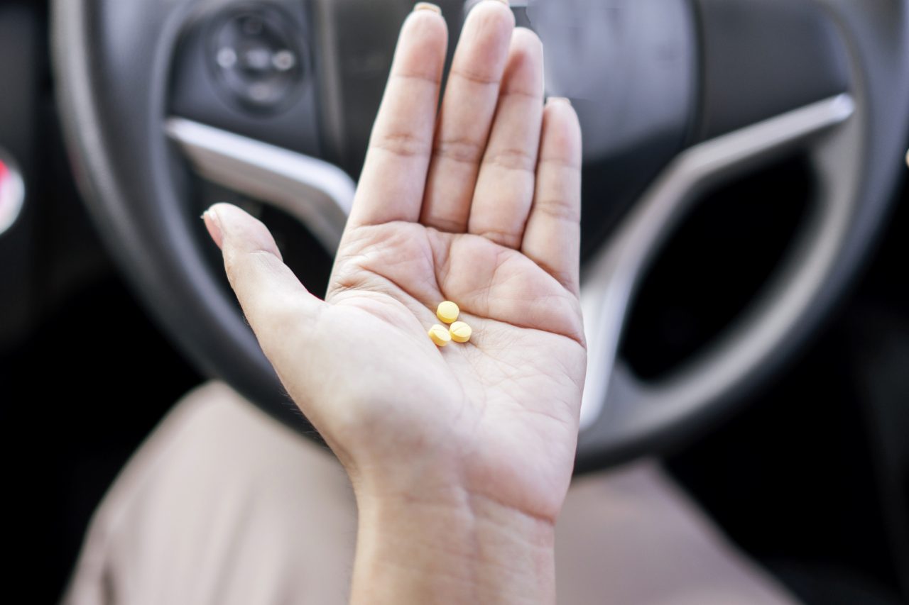 taking medication before driving concept with the woman hand holding allergies pills behind the steering wheel