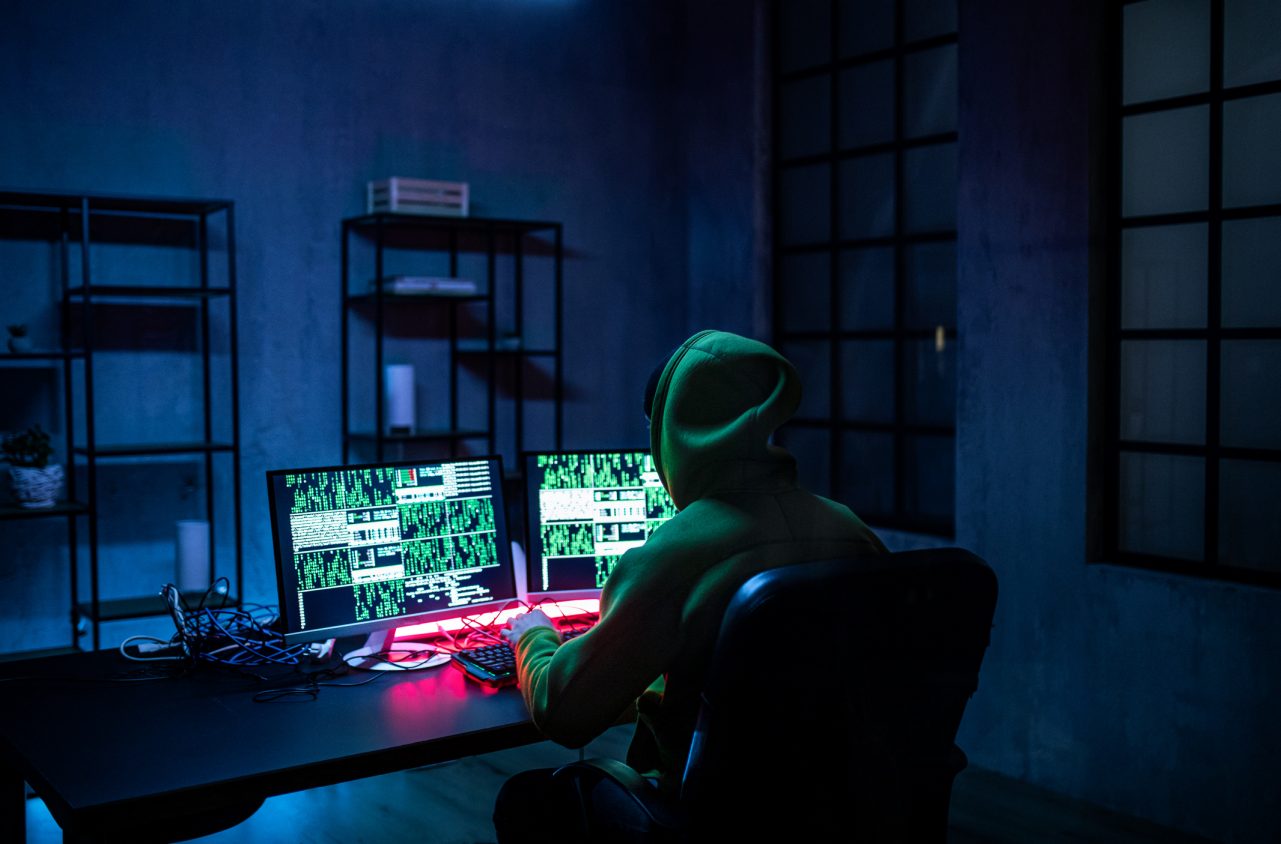 Hacker man working on computers alone in dark room, rear view.