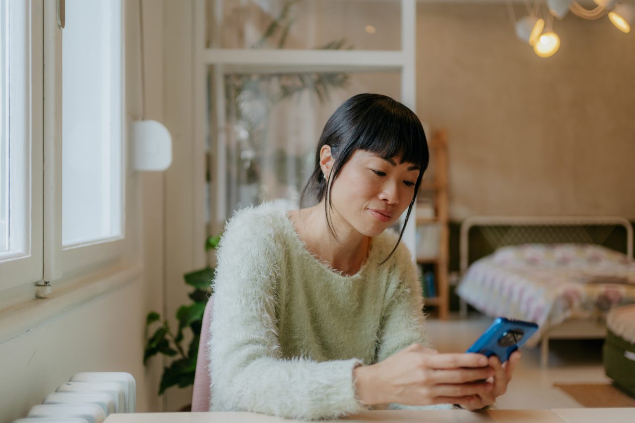 Portrait of a beautiful Japanese woman in her apartment reading morning news online