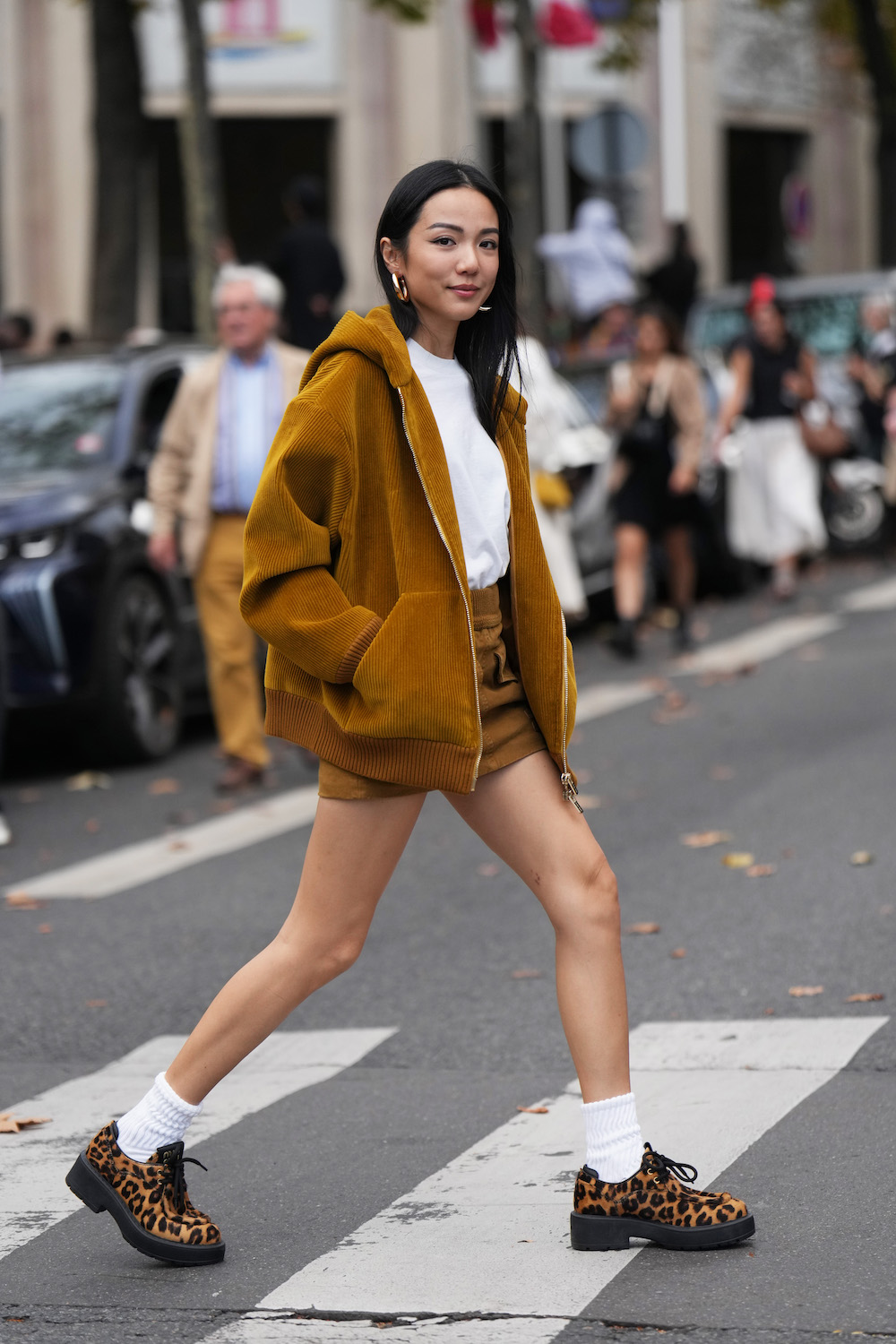 PARIS, FRANCE - OCTOBER 03: Yoyo Cao wears earrings, a brown / orange corduroy hoodie jacket, a white top, matching short mini skirt, white ribbed socks, brown leopard print shoes, outside Miu Miu, during the Womenswear Spring/Summer 2024 as part of  Paris Fashion Week on October 03, 2023 in Paris, France. (Photo by Edward Berthelot/Getty Images)