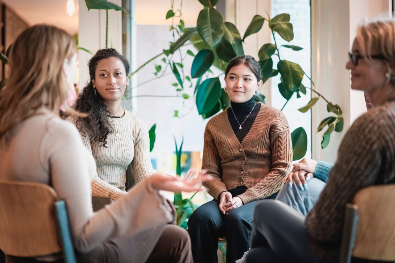 Woman sharing her experiences during a mental health group therapy meeting. Multiracial women participate in support group session sitting in a circle.