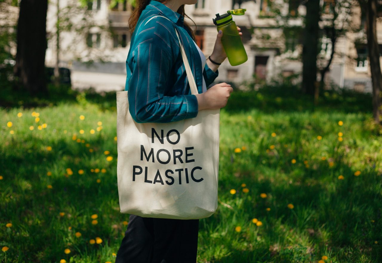 Woman holding reusable cotton zero waste bag with text No More Plastic. Outdoors portrait in sunny day. Eco friendly bags concept.